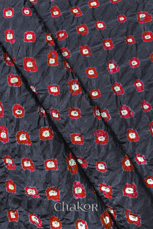 Charcoal Grey Mulberry silk fabric showcasing dual colour Red bandhani patterns with folds and Chakor brand watermark.
