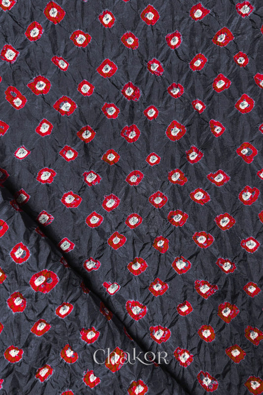 Charcoal Grey Mulberry silk fabric showcasing dual colour Red bandhani patterns with folded corner and Chakor brand watermark.

