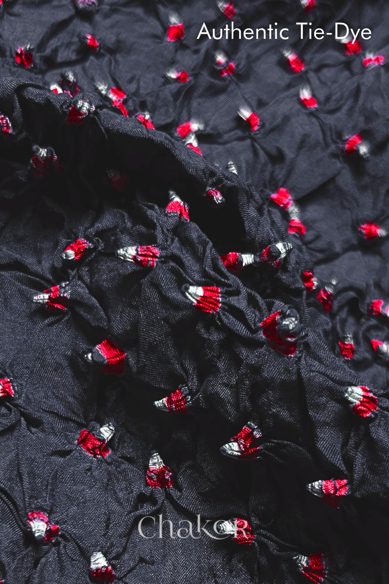 Close-up of Charcoal Grey mulberry silk fabric with Red and white patterns, featuring texture of authentic bandhani patterns.
