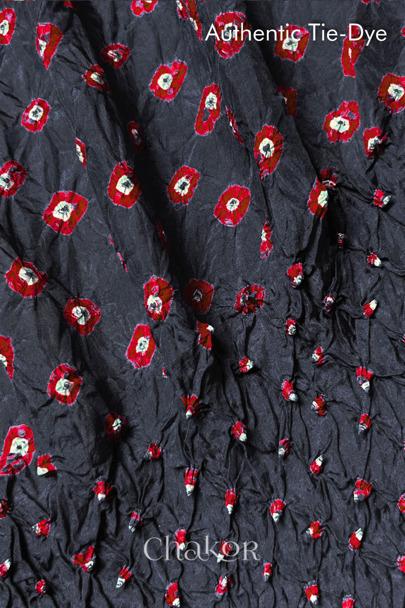 Close-up of Charcoal Grey mulberry silk fabric with Red and white patterns, featuring texture of authentic bandhani patterns.
