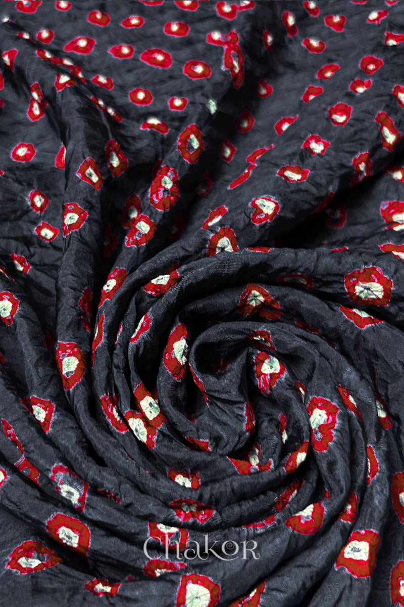 Charcoal Grey Mulberry silk fabric with dual colour Red bandhani dots, arranged in a swirling design  & Chakor brand watermark.
