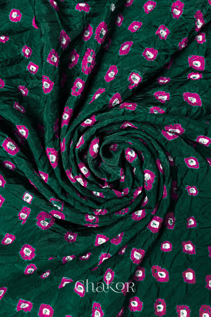 Dark Green Mulberry silk fabric with dual colour Pink bandhani dots, arranged in a swirling design  & Chakor brand watermark.
