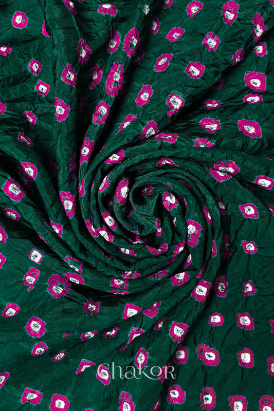 Dark Green Mulberry silk fabric with dual colour Pink bandhani dots, arranged in a swirling design  & Chakor brand watermark.
