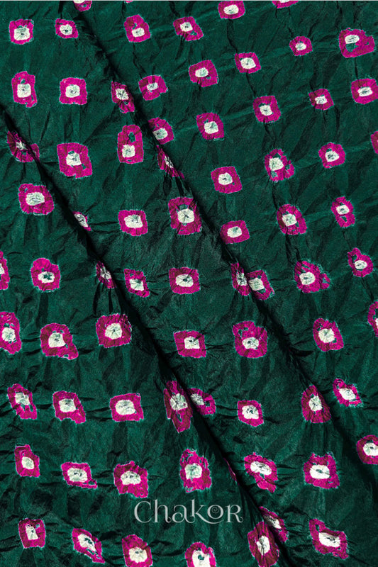 Dark Green Mulberry silk fabric showcasing dual colour Pink bandhani patterns with folds and Chakor brand watermark.
