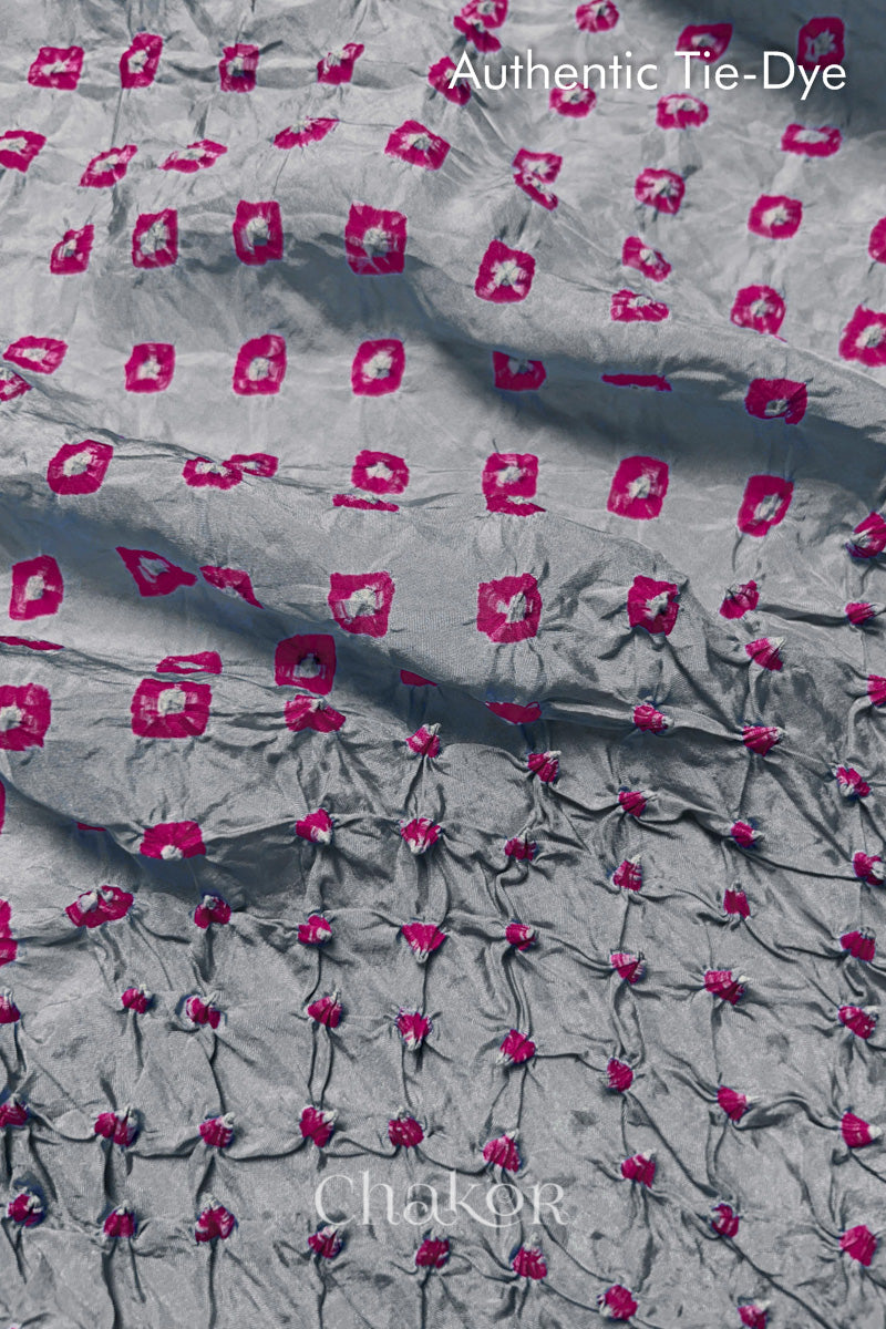 Close-up of Light Grey mulberry silk fabric with Pink and white patterns, featuring texture of authentic bandhani patterns.
