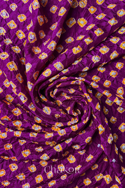 Magenta Mulberry silk fabric with dual colour Yellow bandhani dots, arranged in a swirling design  & Chakor brand watermark.
