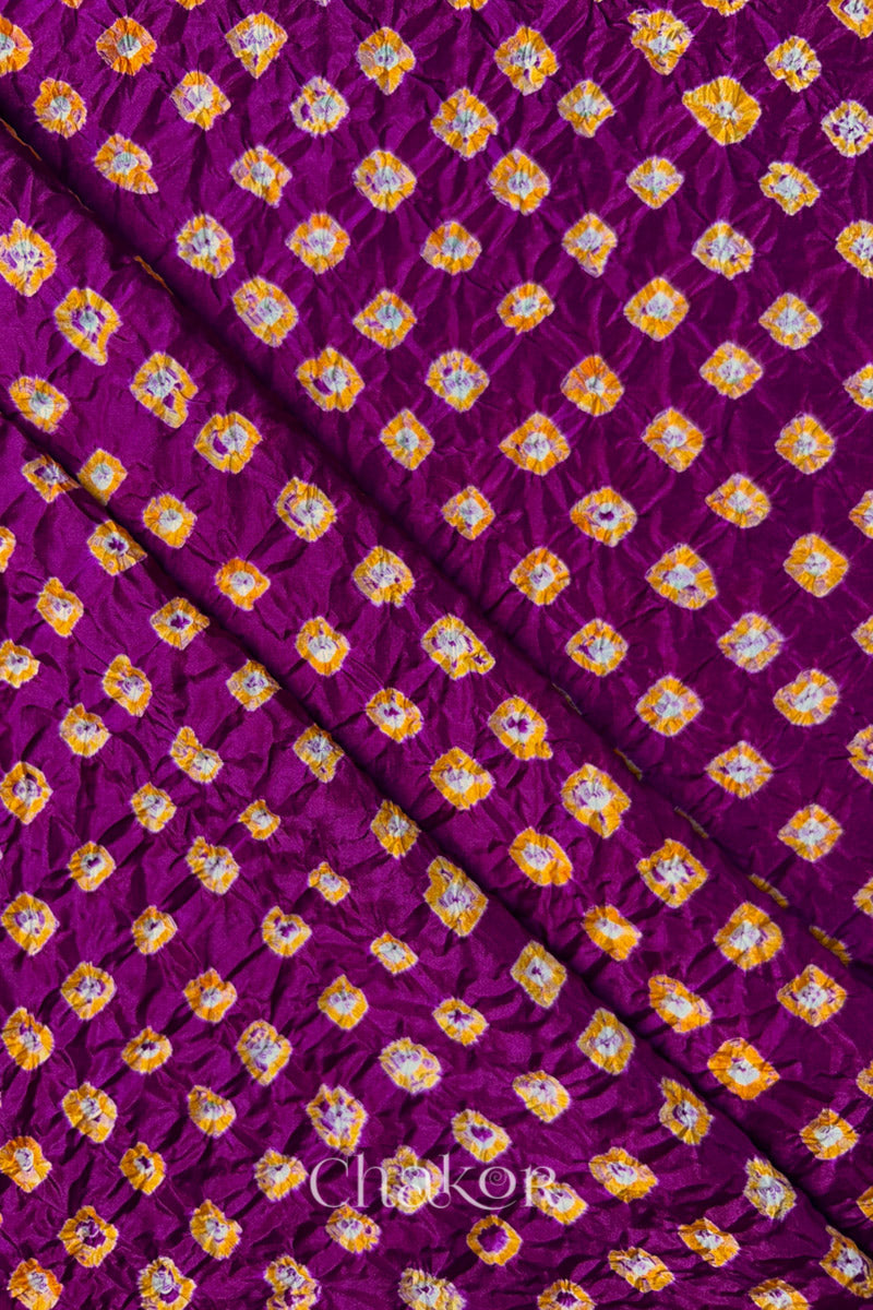 Magenta Mulberry silk fabric showcasing dual colour Yellow bandhani patterns with folds and Chakor brand watermark.

