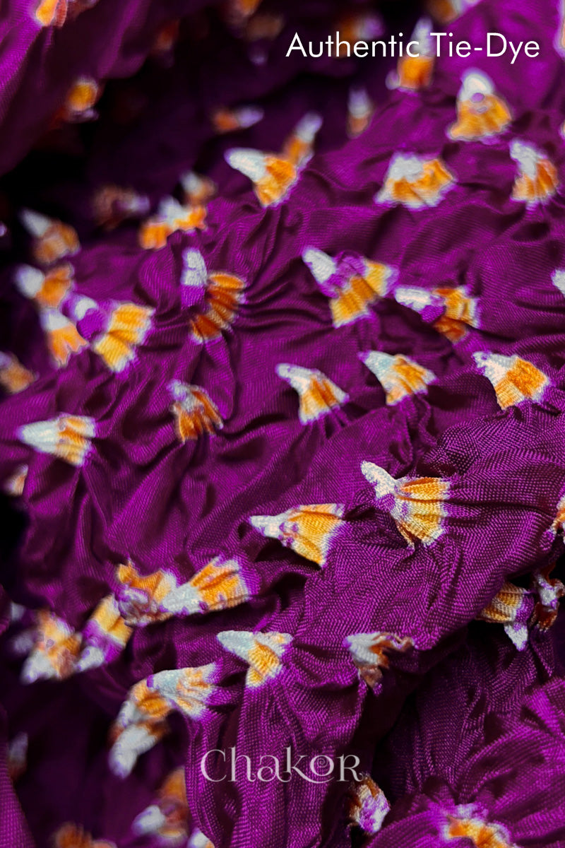Close-up of Magenta mulberry silk fabric with Yellow and white patterns, featuring texture of authentic bandhani patterns.
