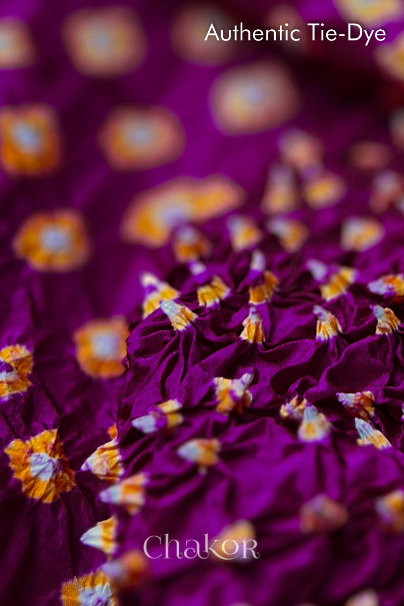 Close-up of Magenta mulberry silk fabric with Yellow and white patterns, featuring texture of authentic bandhani patterns.
