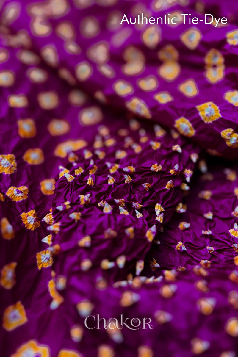 Close-up of Magenta mulberry silk fabric with Yellow and white patterns, featuring texture of authentic bandhani patterns.
