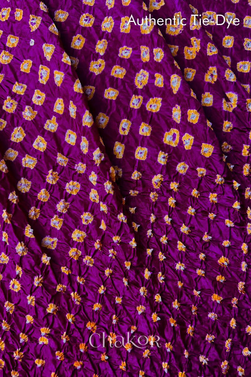 Close-up of Magenta mulberry silk fabric with Yellow and white patterns, featuring texture of authentic bandhani patterns.
