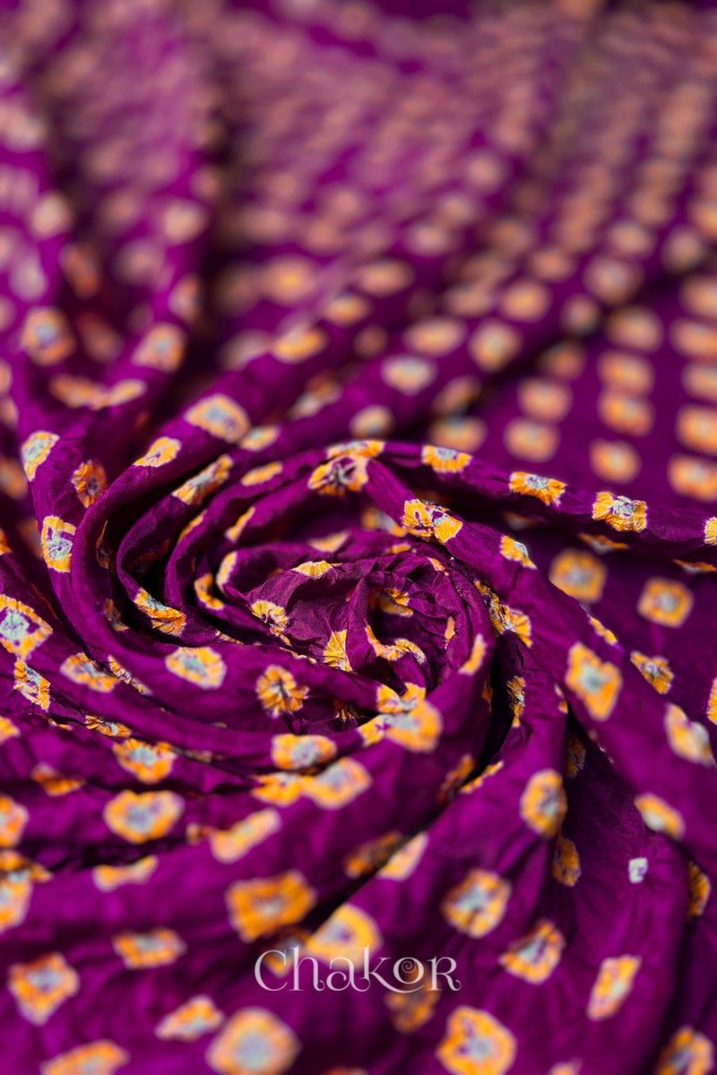 Magenta Mulberry silk fabric with dual colour Yellow bandhani dots, arranged in a swirling design  & Chakor brand watermark.
