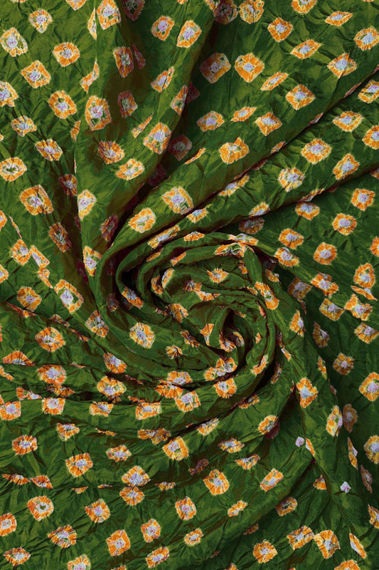 Mehendi Green Mulberry silk fabric with dual colour Yellow bandhani dots, arranged in a swirling design  & Chakor brand watermark.
