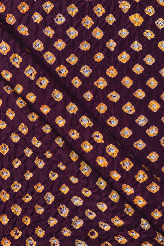 Maroon Mulberry silk fabric showcasing dual colour Yellow bandhani patterns with folds and Chakor brand watermark.
