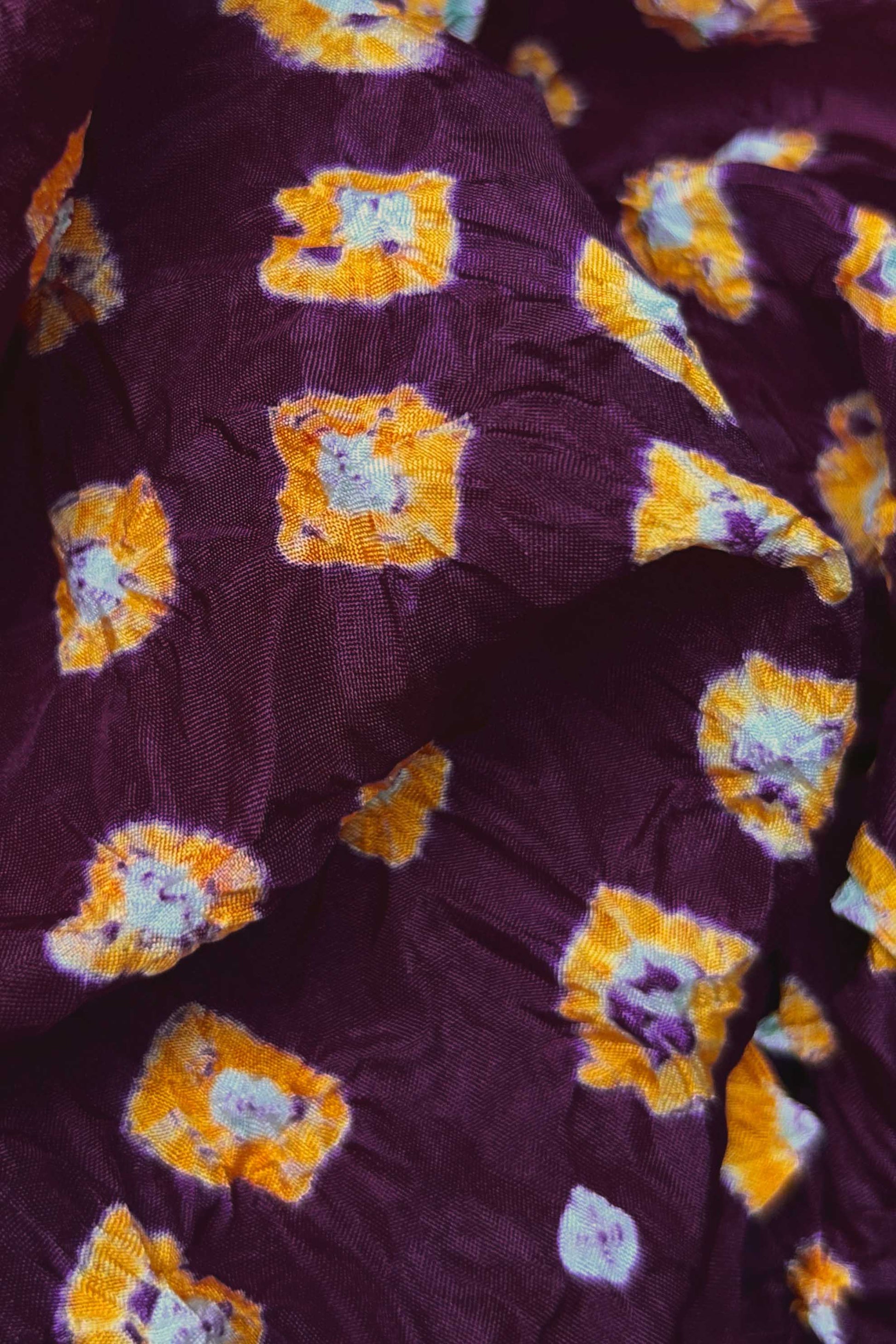Close-up of Maroon fabric with Yellow and white bandhani patterns, featuring texture and sheen of soft mulberry silk fabric.
