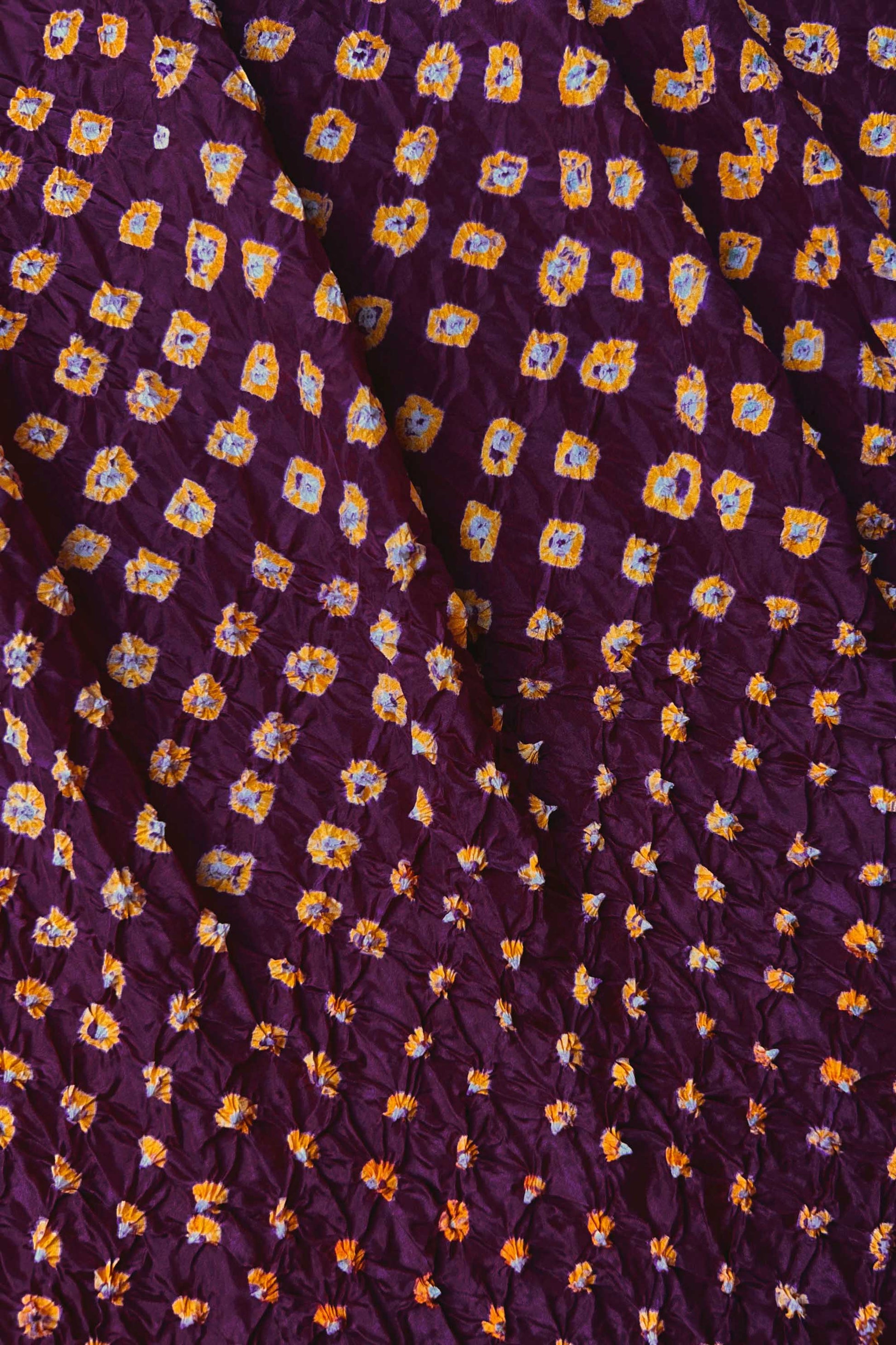 Close-up of Maroon mulberry silk fabric with Yellow and white patterns, featuring texture of authentic bandhani patterns.
