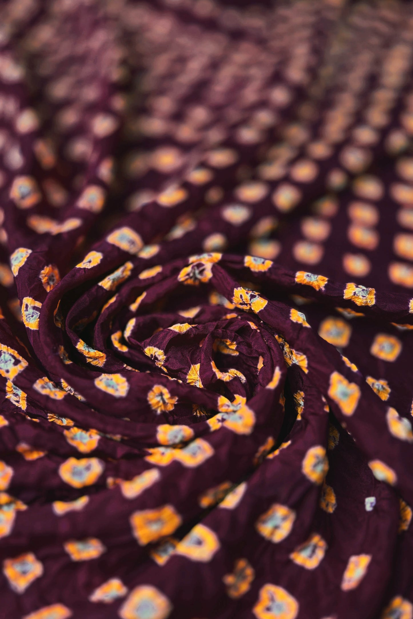 Maroon Mulberry silk fabric with dual colour Yellow bandhani dots, arranged in a swirling design  & Chakor brand watermark.
