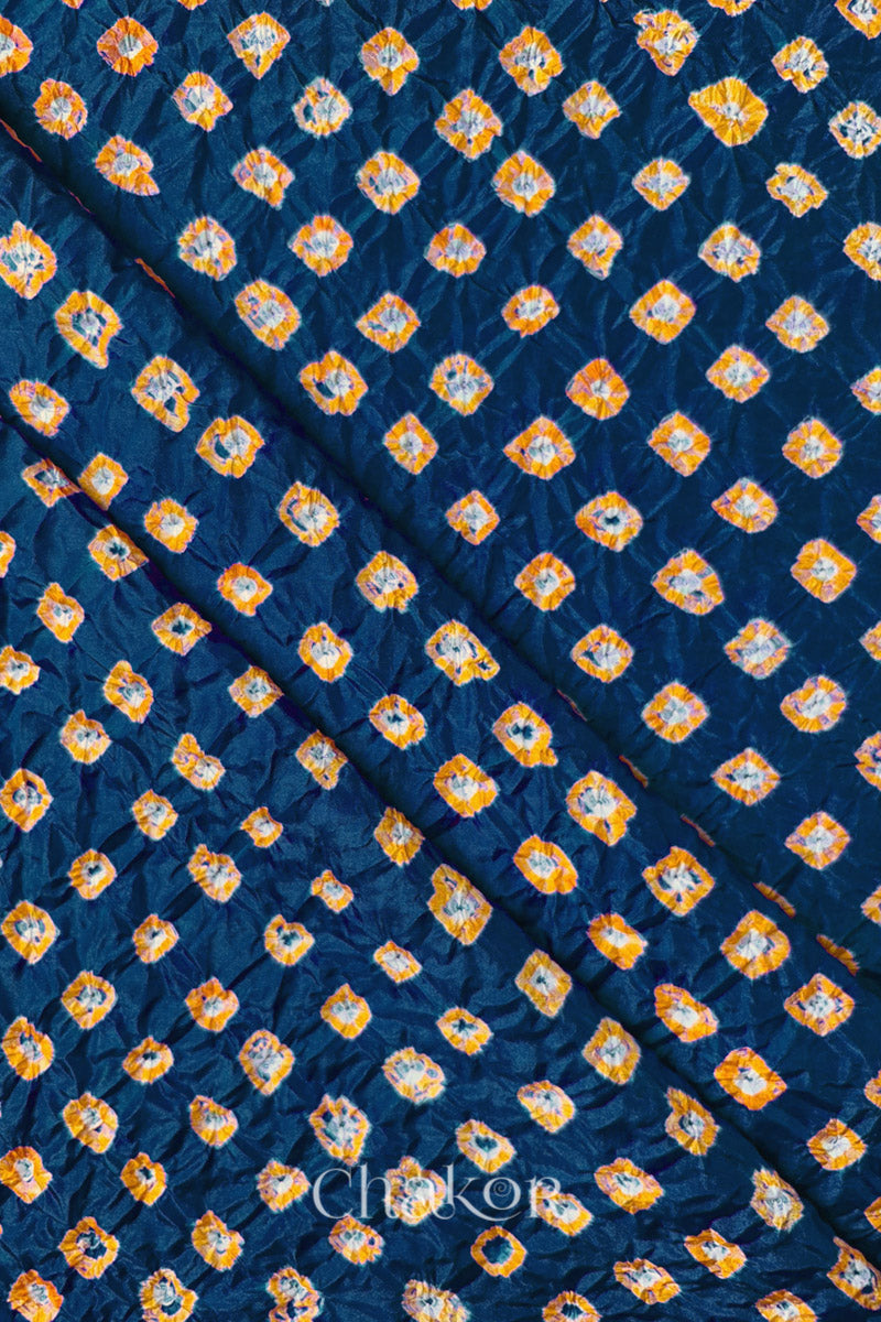 Deep Indigo Mulberry silk fabric showcasing dual colour Yellow bandhani patterns with folds and Chakor brand watermark.
