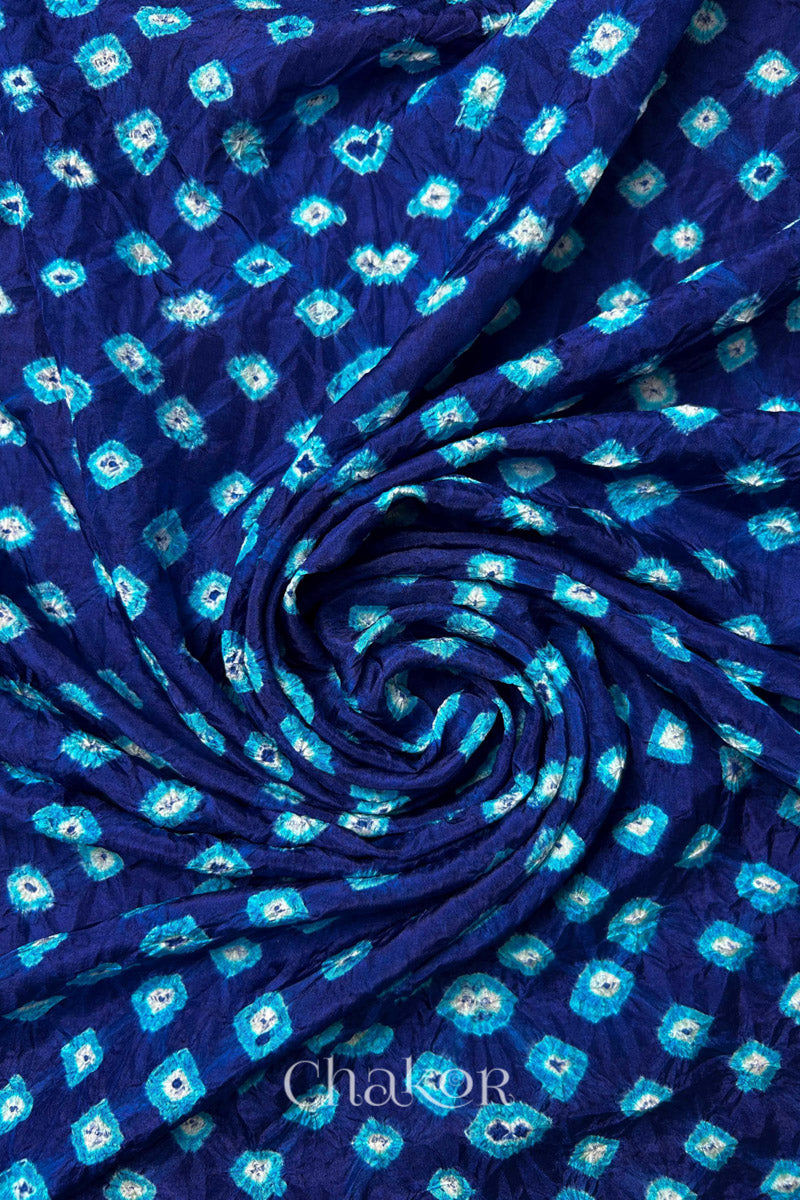 Navy Mulberry silk fabric with dual colour Turquoise Blue bandhani dots, arranged in a swirling design  & Chakor brand watermark.
