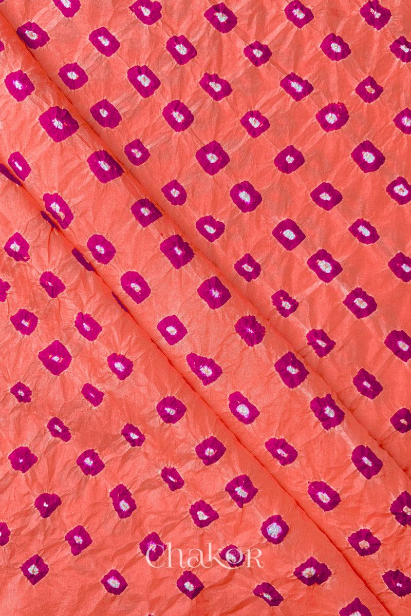 Peach Mulberry silk fabric showcasing dual colour Pink bandhani patterns with folds and Chakor brand watermark.

