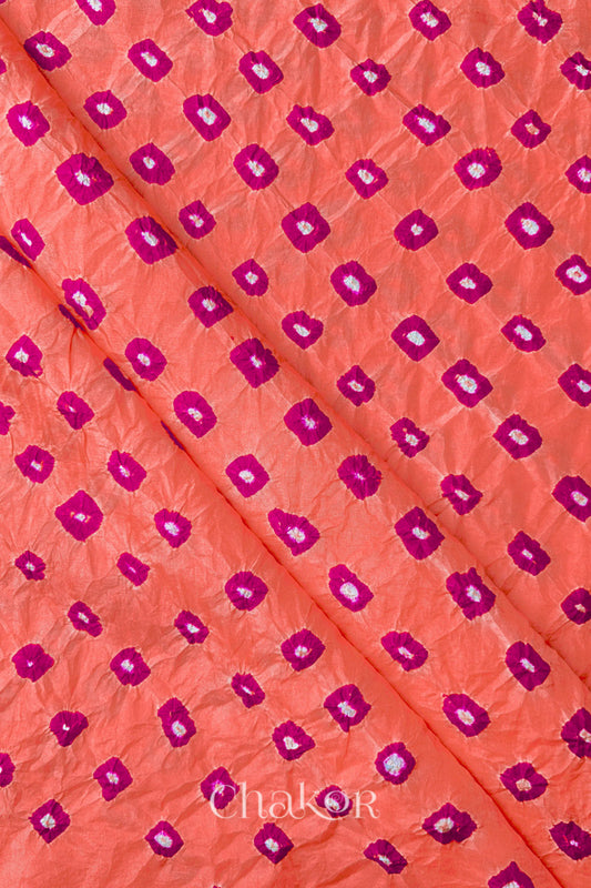 Peach Mulberry silk fabric showcasing dual colour Pink bandhani patterns with folds and Chakor brand watermark.
