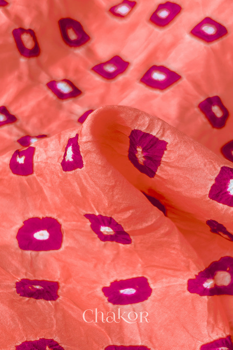 Close-up of Peach fabric with Pink and white bandhani patterns, featuring texture and sheen of soft mulberry silk fabric.
