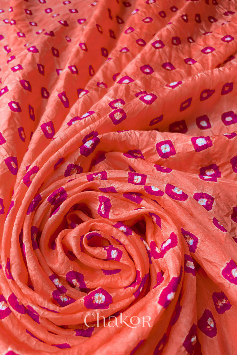 Peach Mulberry silk fabric with dual colour Pink bandhani dots, arranged in a swirling design  & Chakor brand watermark.
