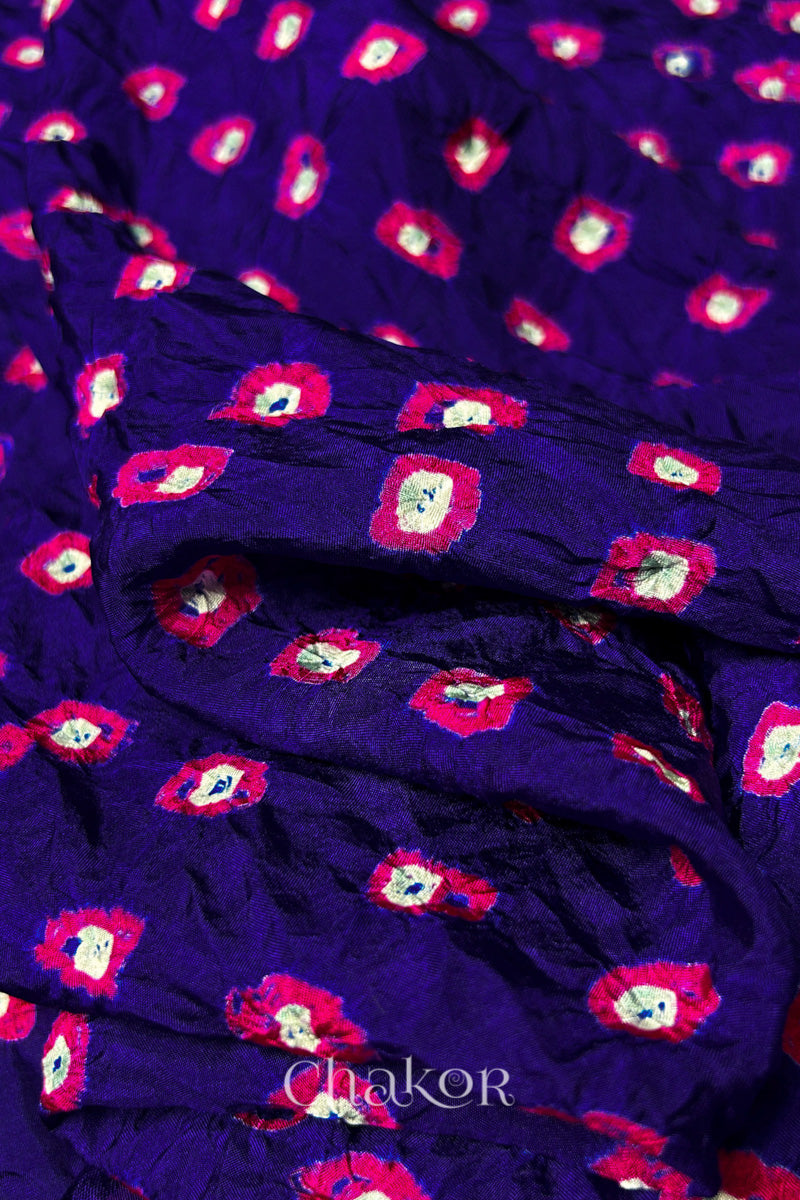 Close-up of Purple fabric with Pink and white bandhani patterns, featuring texture and sheen of soft mulberry silk fabric.
