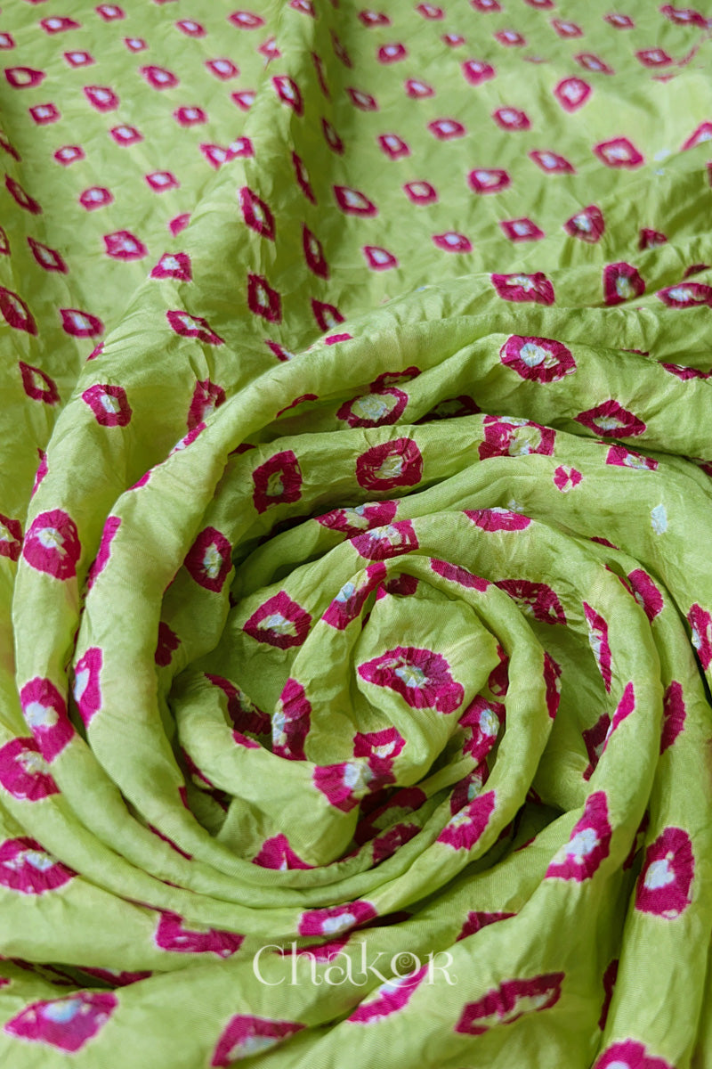Pista Green Mulberry silk fabric with dual colour Pink bandhani dots, arranged in a swirling design  & Chakor brand watermark.
