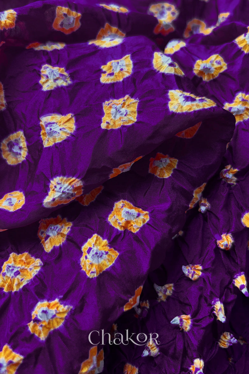 Close-up of Purple fabric with Yellow and white bandhani patterns, featuring texture and sheen of soft mulberry silk fabric.
