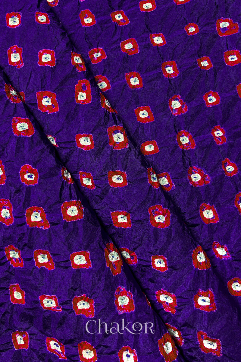 Purple Mulberry silk fabric showcasing dual colour Red bandhani patterns with folds and Chakor brand watermark.

