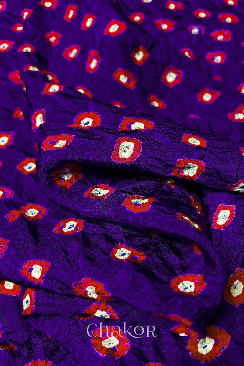 Close-up of Purple fabric with Red and white bandhani patterns, featuring texture and sheen of soft mulberry silk fabric.
