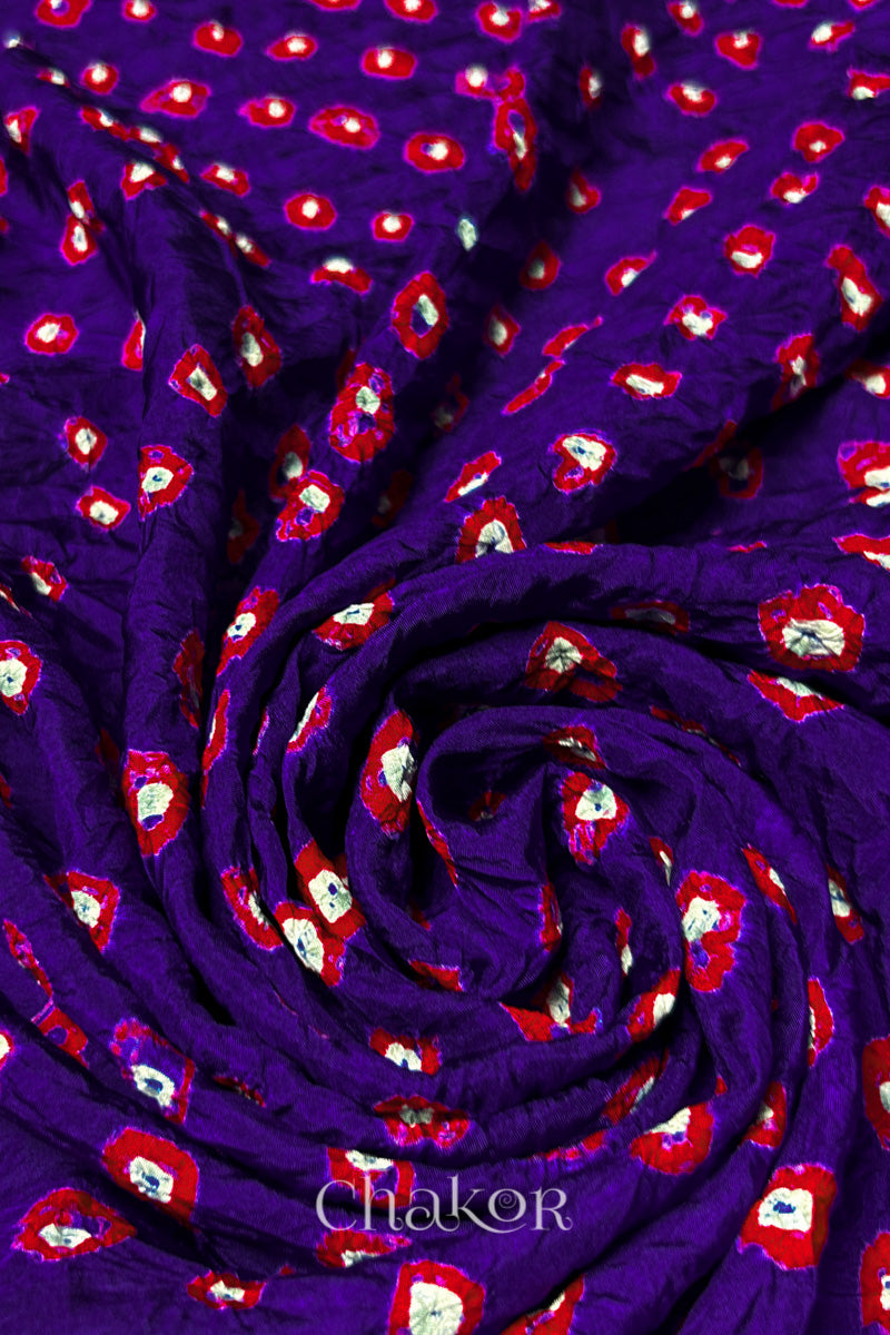 Purple Mulberry silk fabric with dual colour Red bandhani dots, arranged in a swirling design  & Chakor brand watermark.
