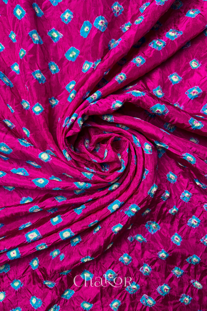 Rani Pink Mulberry silk fabric with dual colour Turquoise Blue bandhani dots, arranged in a swirling design  & Chakor brand watermark.
