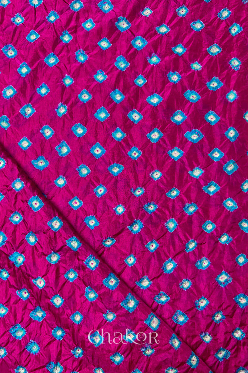 Rani Pink Mulberry silk fabric showcasing dual colour Turquoise Blue bandhani patterns with folded corner and Chakor brand watermark.
