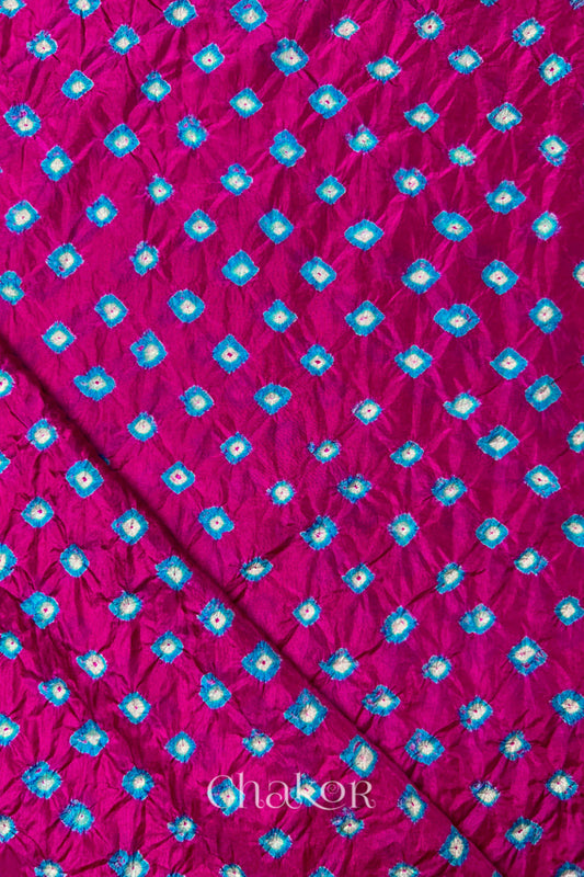 Rani Pink Mulberry silk fabric showcasing dual colour Turquoise Blue bandhani patterns with folded corner and Chakor brand watermark.
