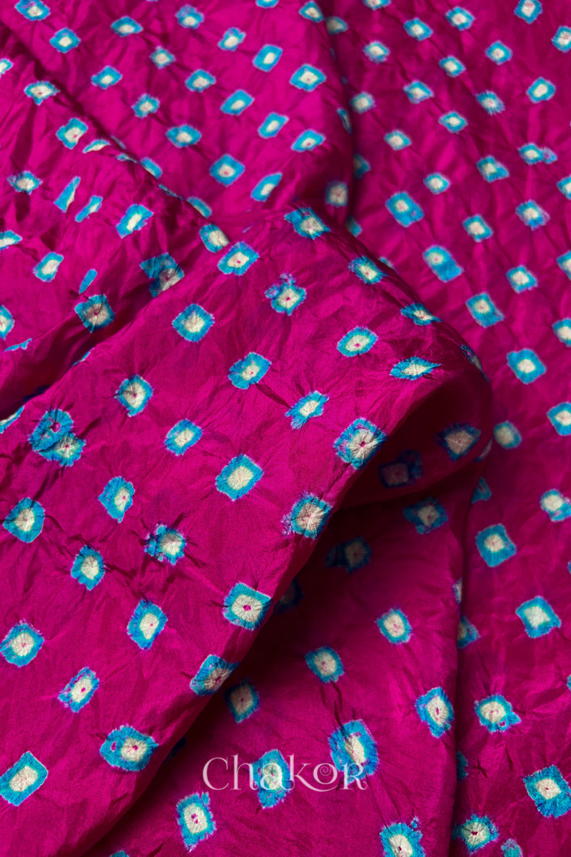 Close-up of Rani Pink fabric with Turquoise Blue and white bandhani patterns, featuring texture and sheen of soft mulberry silk fabric.
