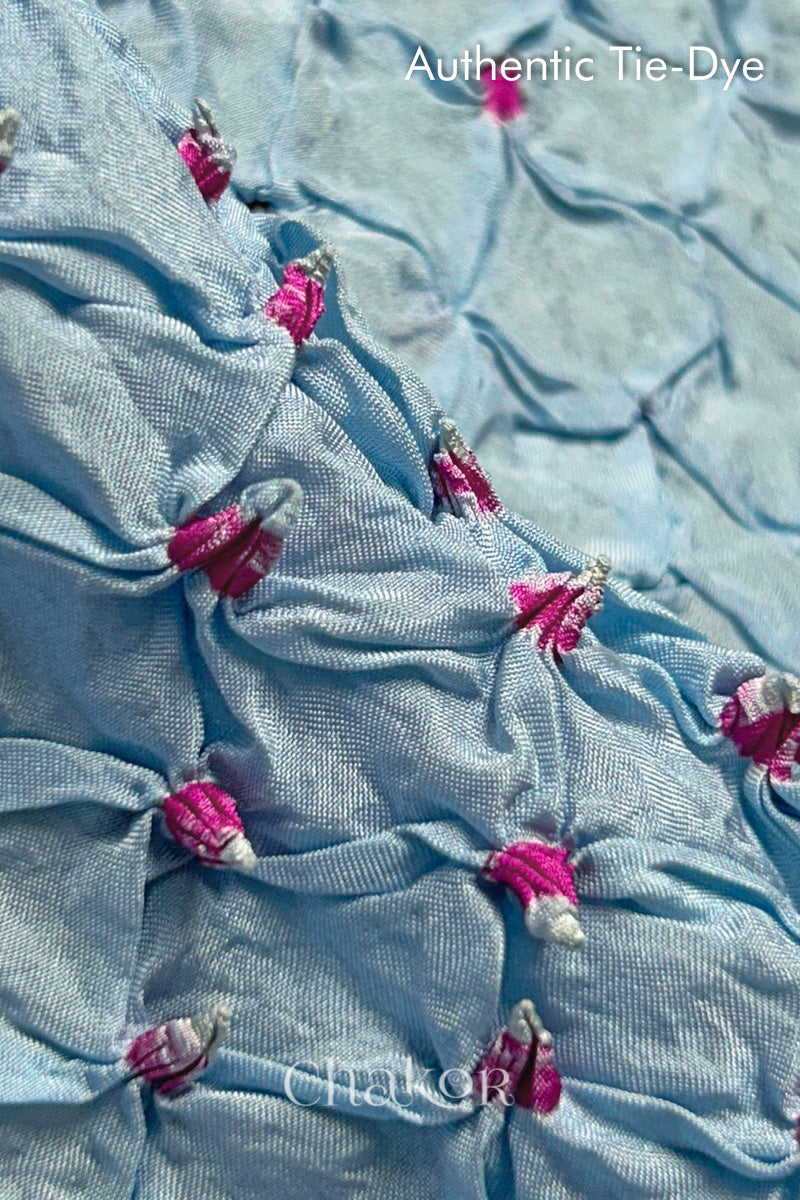 Close-up of Sky Blue mulberry silk fabric with Pink and white patterns, featuring texture of authentic bandhani patterns.
