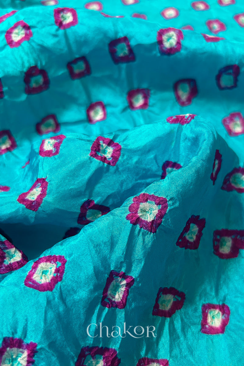 Close-up of Turquoise Blue fabric with Pink and white bandhani patterns, featuring texture and sheen of soft mulberry silk fabric.
