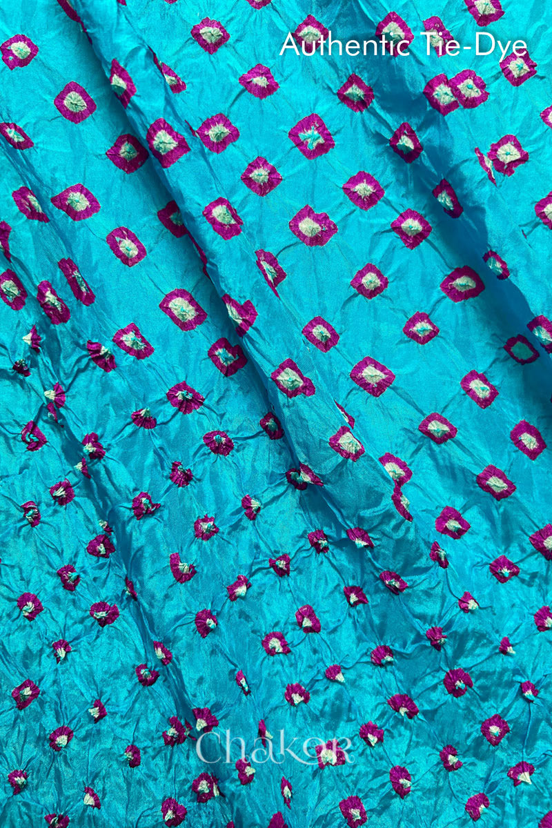 Close-up of Turquoise Blue mulberry silk fabric with Pink and white patterns, featuring texture of authentic bandhani patterns.
