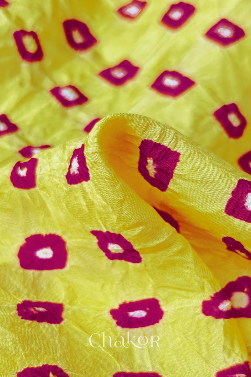 Close-up of yellow fabric with Pink and white bandhani patterns, featuring texture and sheen of soft mulberry silk fabric.
