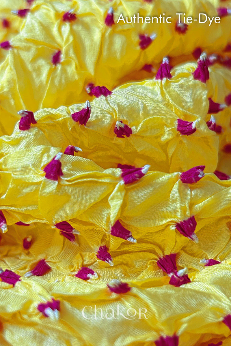 Close-up of yellow mulberry silk fabric with Pink and white patterns, featuring texture of authentic bandhani patterns.
