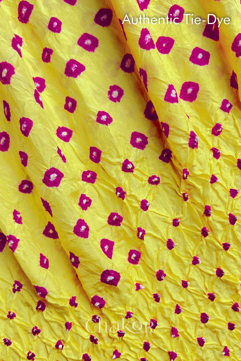 Close-up of yellow mulberry silk fabric with Pink and white patterns, featuring texture of authentic bandhani patterns.
