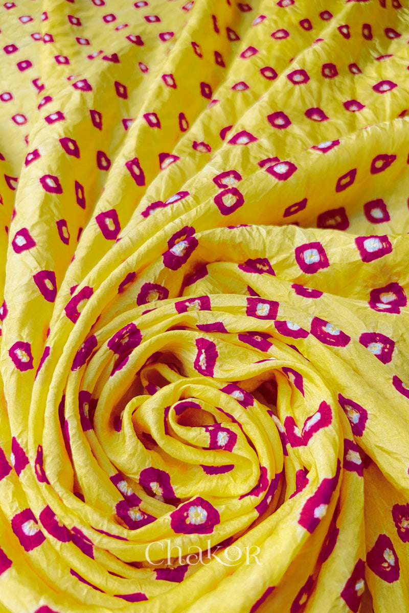 Yellow Pink Mulberry silk fabric with dual colour Pink bandhani dots, arranged in a swirling design  & Chakor brand watermark.
