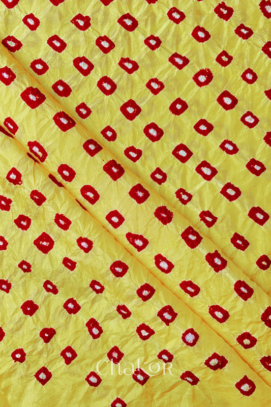Yellow Red Mulberry silk fabric showcasing dual coloured bandhani patterns with folds and Chakor brand watermark.