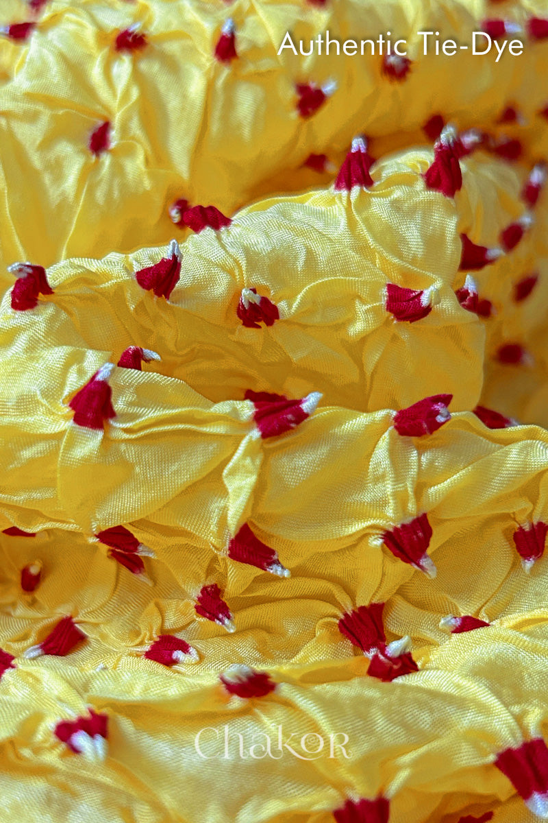 Close-up of yellow mulberry silk fabric with red and white patterns, featuring texture of authentic bandhani patterns.
