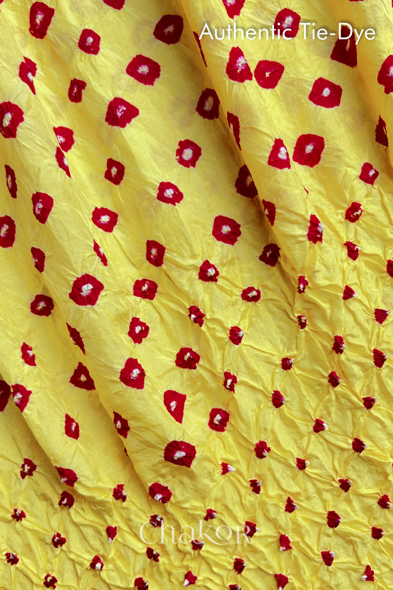 Close-up of yellow mulberry silk fabric with red and white patterns, featuring texture of authentic bandhani patterns.